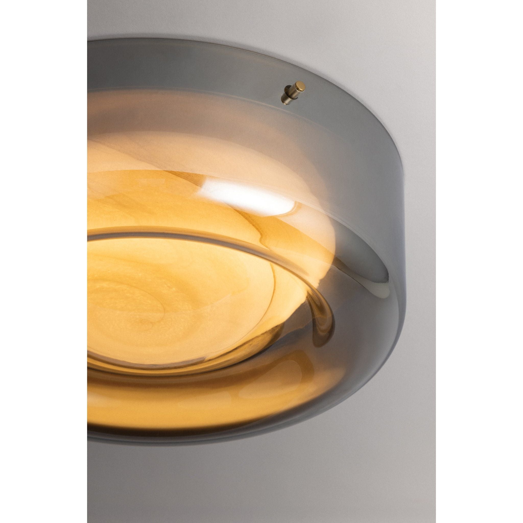 Close-up detail of round flush mount ceiling light showing layered amber glass diffuser disc in gunmetal grey frame