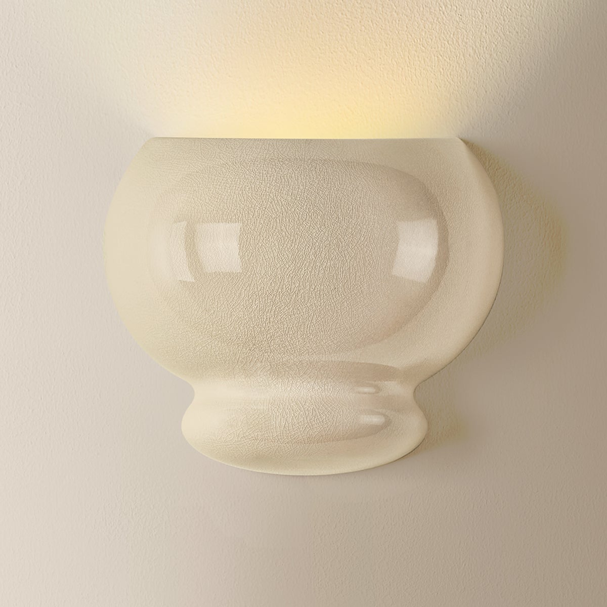 White ceramic bubble wall sconce mounted on wall, emitting warm upward light