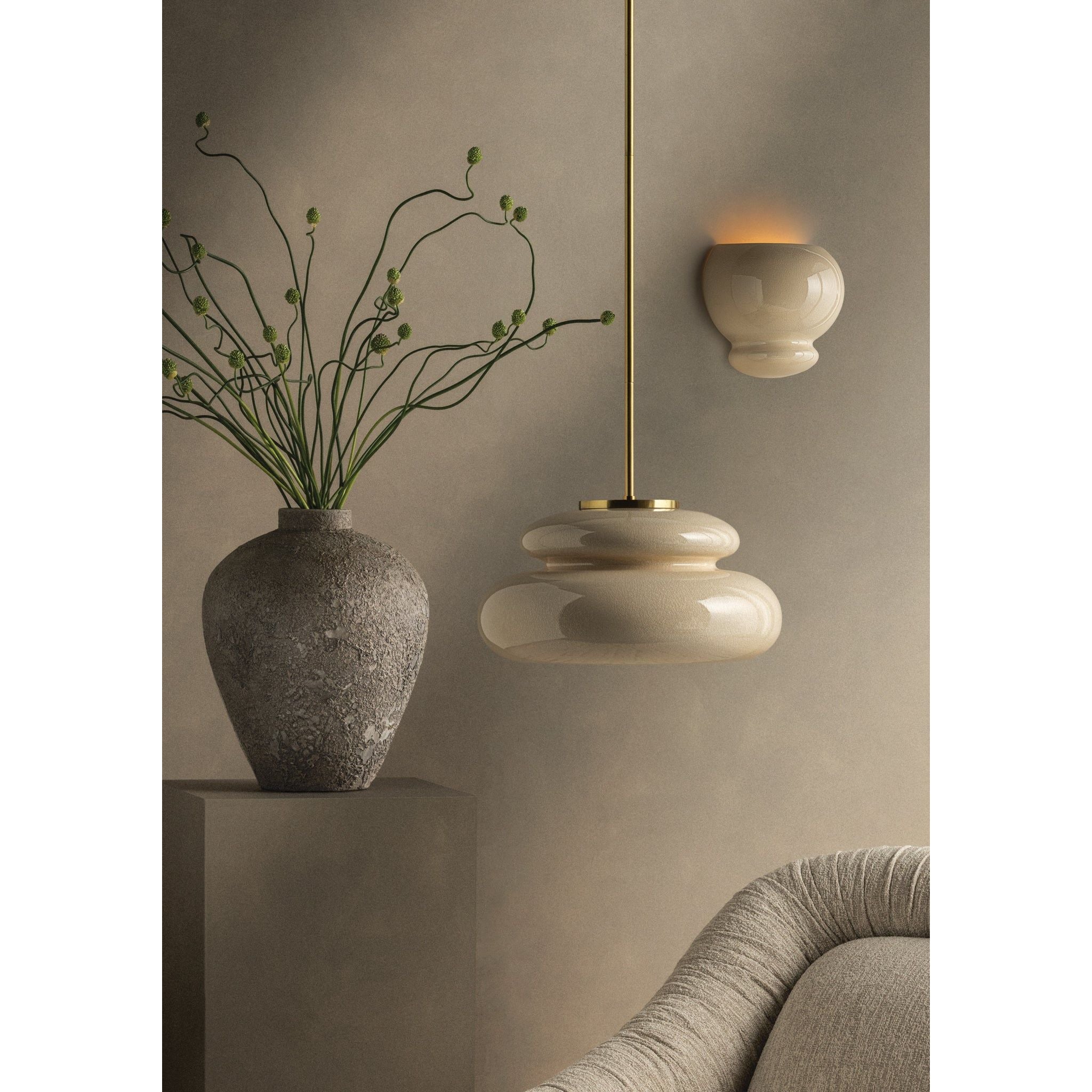 Styled room scene with cream disc pendant light on brass rod and ceramic bubble wall sconce, beside a vase with branches