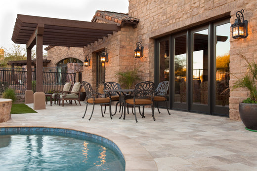 Outdoor lighting trends with lantern-style outdoor light fixtures on a stone wall, brightening a patio with a pergola and stylish furniture.