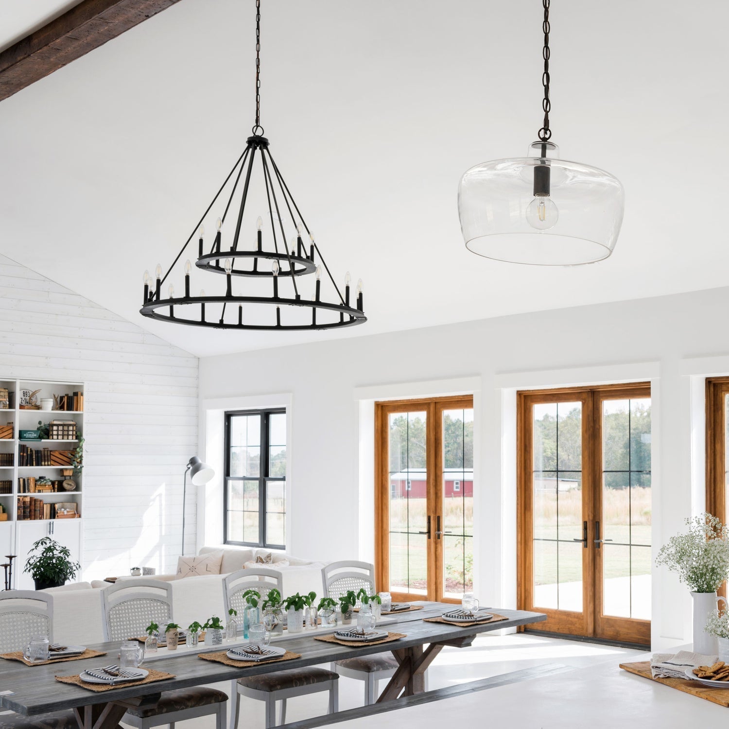Dining area featuring a black chandelier with a modern farmhouse design and a smaller pendant light, highlighting natural light and rustic decor.
