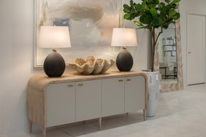 Elegant console table with two black table lamps, a decorative shell bowl centerpiece, and abstract wall art, complemented by a fiddle leaf fig in a stylish pot.