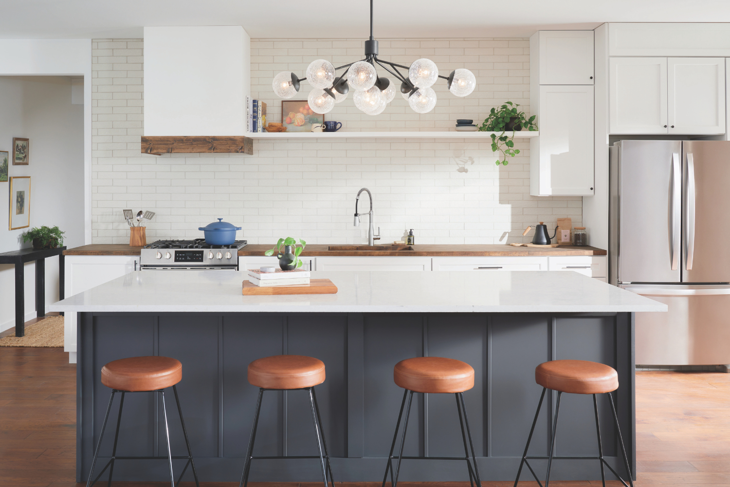 Modern kitchen with a black chandelier and white island with leather stools.
