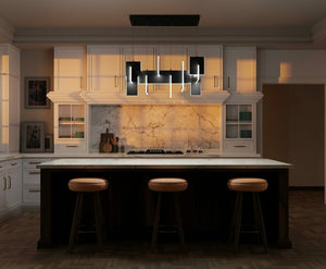 Modern kitchen interior with a large marble island and a sleek, contemporary chandelier by Eurofase Lighting hanging above. The room features white cabinetry, marble backsplash, and warm ambient lighting, creating a stylish and inviting atmosphere.