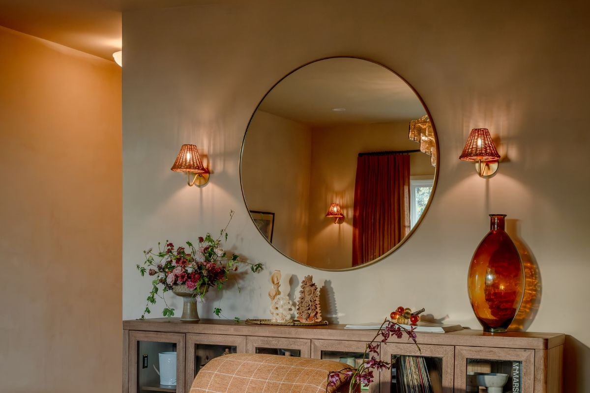 Wall sconces beside a round mirror above a console table showing wall sconce lighting mixtakes in placement and bulb warmth