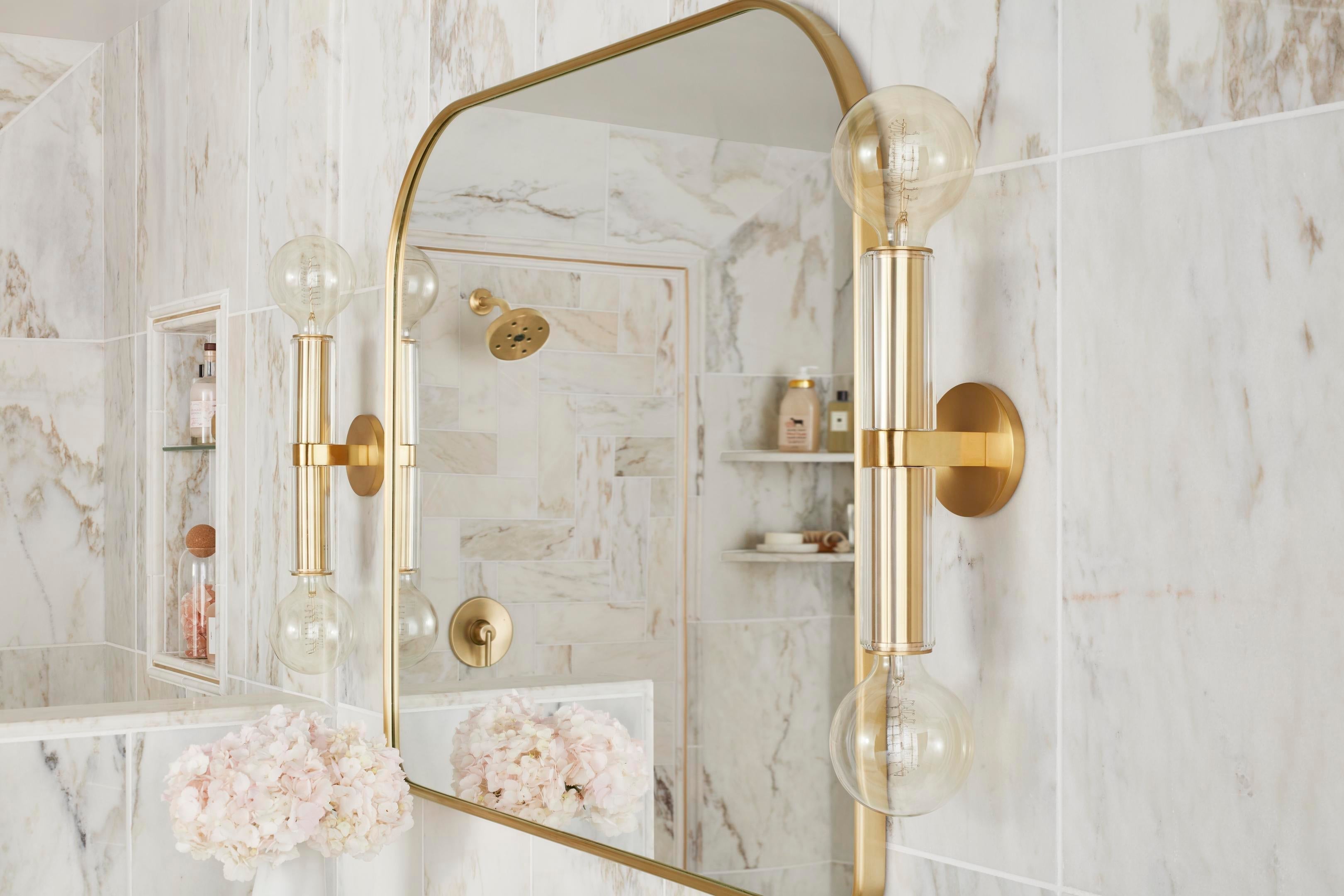 Brushed gold vertical vanity light fixtures beside the bathroom mirror providing even illumination in a luxurious marble bathroom