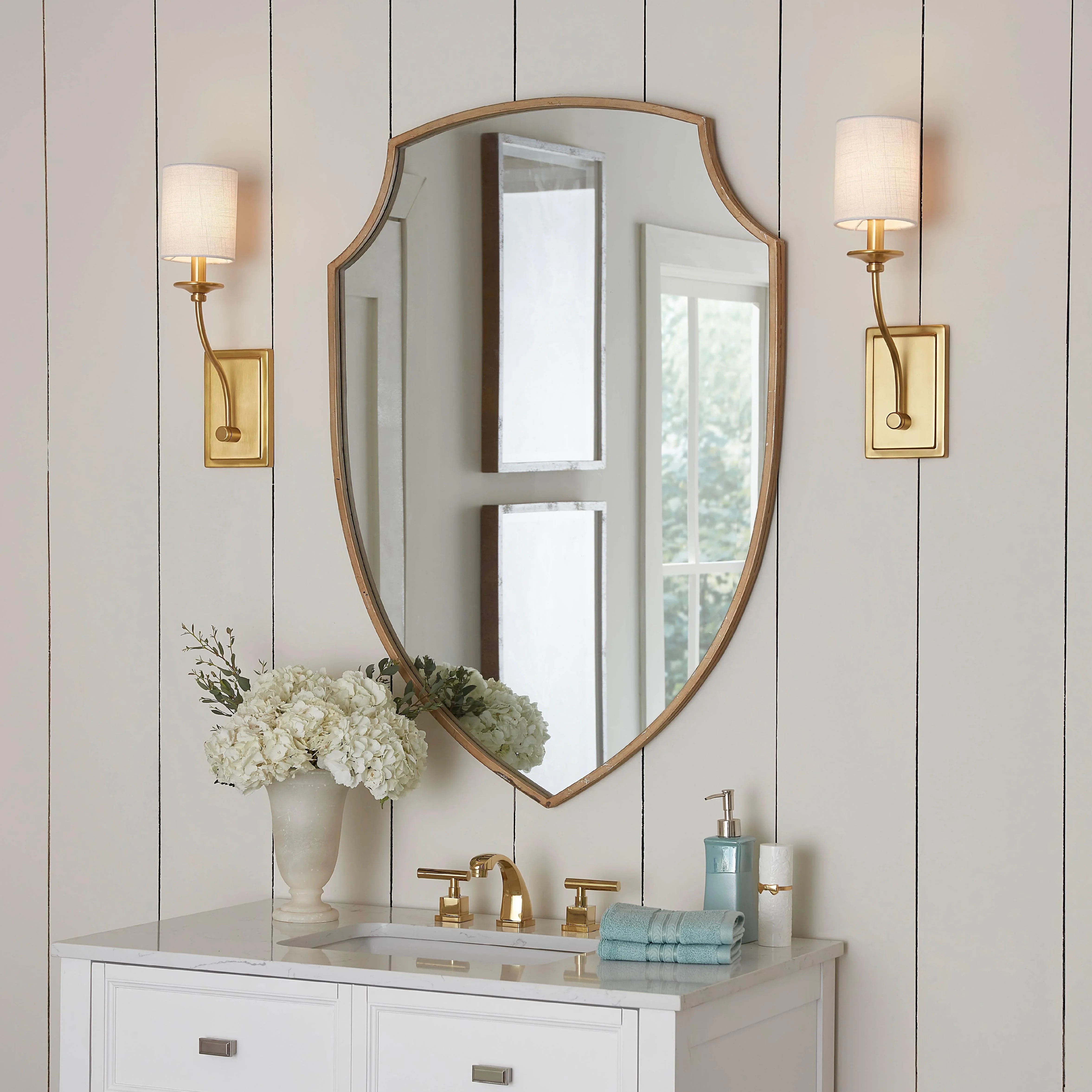 Sale wall lights with gold bases and white fabric shades mounted beside a bathroom mirror.