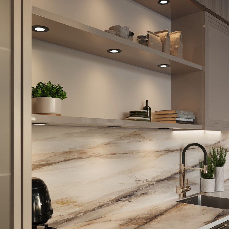 Black recessed puck lights installed under open kitchen shelves, providing focused task lighting over a marble backsplash and countertop.