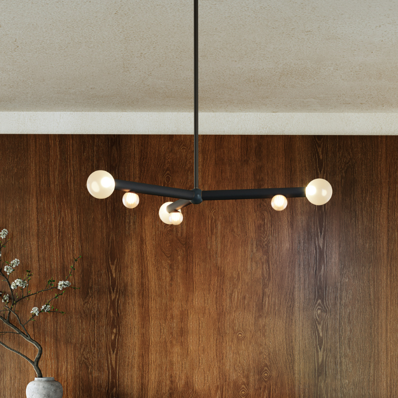 Modern black linear chandelier with round white globe lights against a dark wood accent wall.
