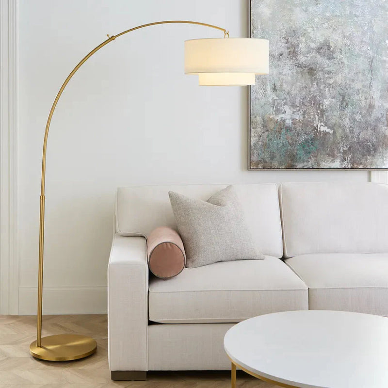 Arc Floor Lamp brass arc floor lamp with layered white drum shade over a light living room sofa.