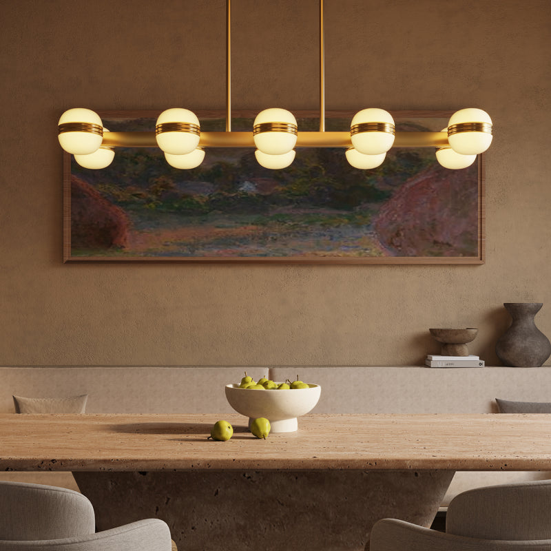 Kuzco modern linear chandelier with glowing globe lights and brass details suspended above a dining table.
