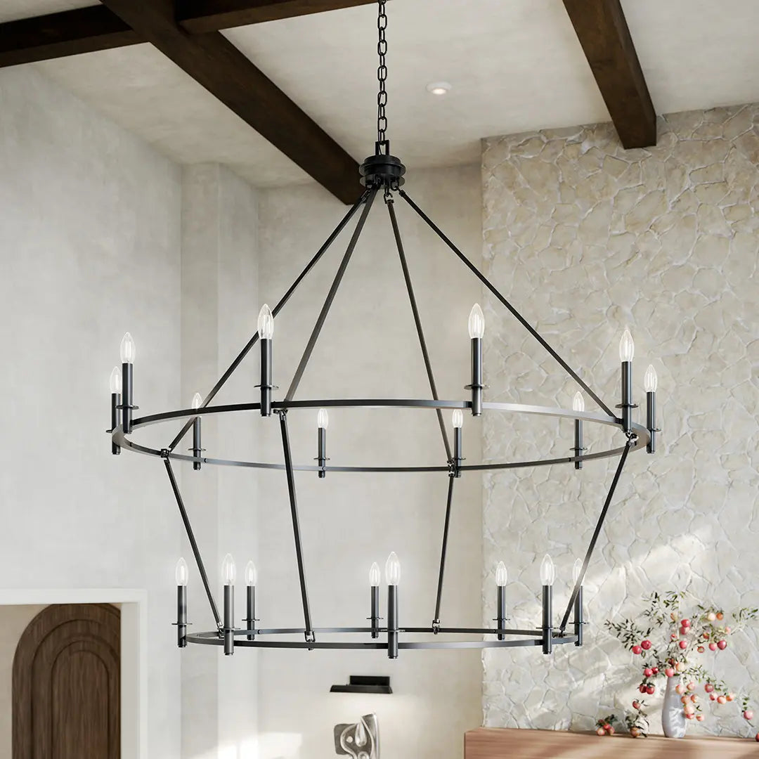 Large two-tier black iron candle chandelier in a rustic dining space with exposed beams and stone walls.