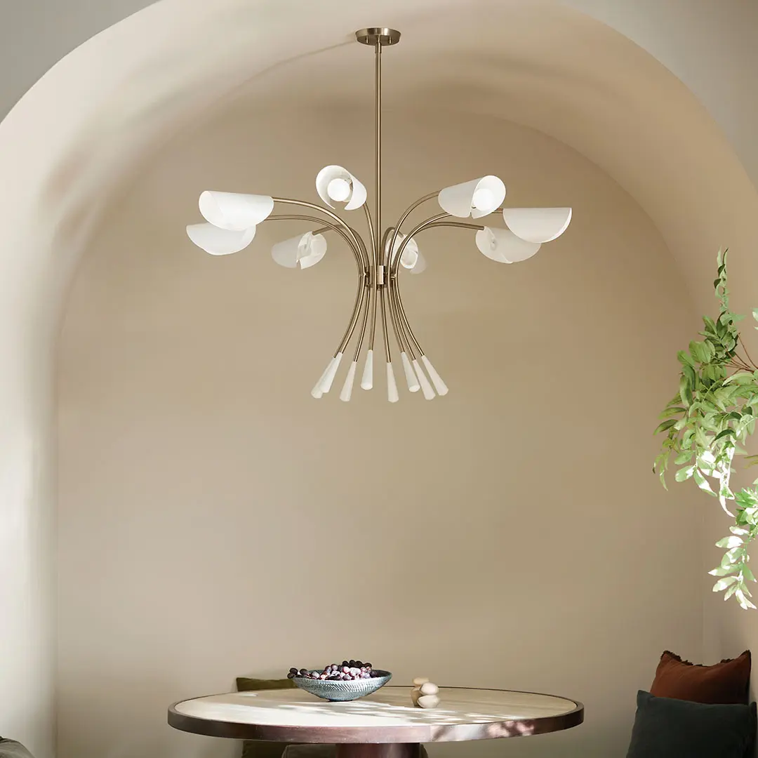 Kichler sculptural chandelier with curved brass arms and white glass shades hanging in an arched dining nook.