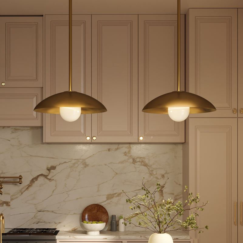 Pendant Lights brass dome pendant lights hanging above a beige kitchen with marble backsplash.