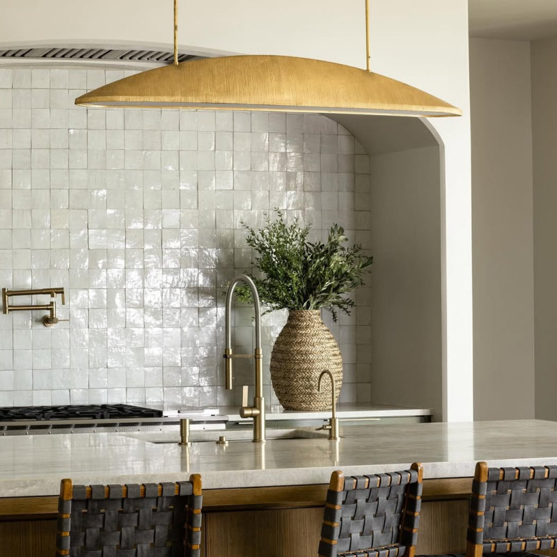 Visual Comfort & Co. large gold linear pendant light hanging above a kitchen island with white tile backsplash and brass fixtures.
