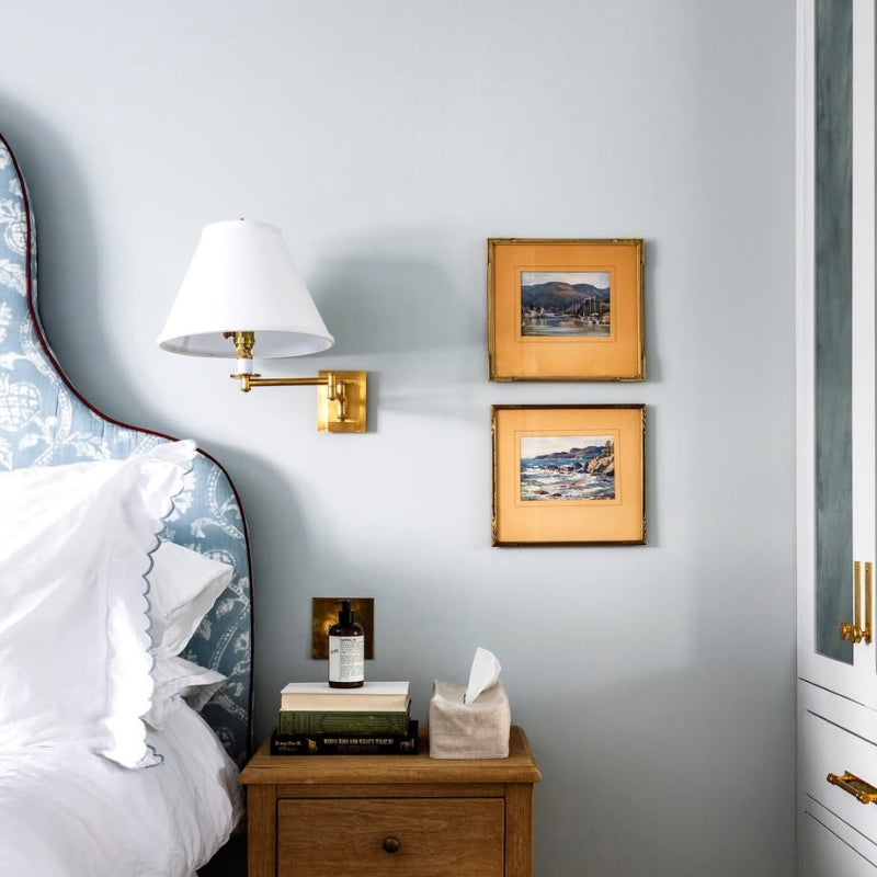Swing Arms brass swing arm wall lamp with white shade beside a bedroom nightstand.