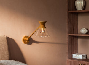 Scandinavian lighting with a minimalist wall sconce featuring a gold finish and glass shade, adding sleek style to a modern bedroom.