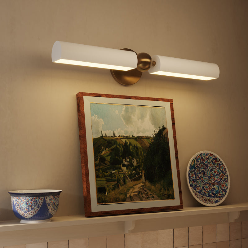 Modern brass and white picture light mounted above framed artwork, casting warm illumination over a decorative shelf.