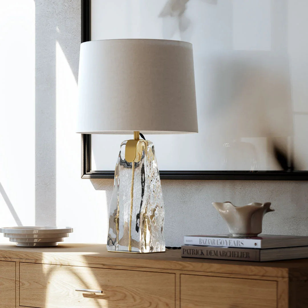 Elegant glass table lamp with a textured clear base and fabric shade, placed on a wooden console table.