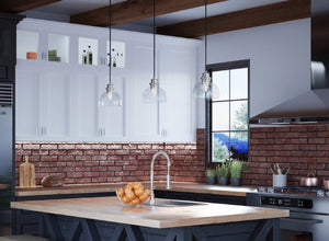 Modern industrial kitchen lighting with clear glass pendants over a wood island, exposed brick backsplash, and steel accents.