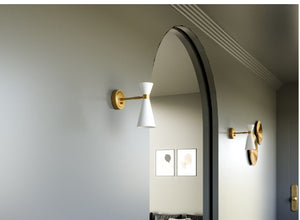 Mid-century modern wall sconces with brass and white finishes, illuminating a minimalist hallway with an arched doorway.