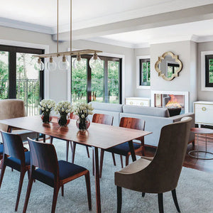 Linear chandelier with clear globe lights hanging over a dining table in a modern open-concept living and dining area, available at Lights Canada.