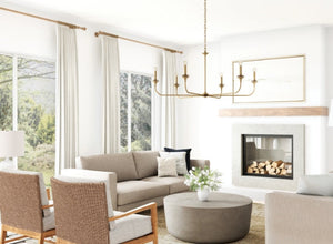 Living room lighting with a minimalist brass chandelier, bright neutral decor, and large windows bringing in natural light.