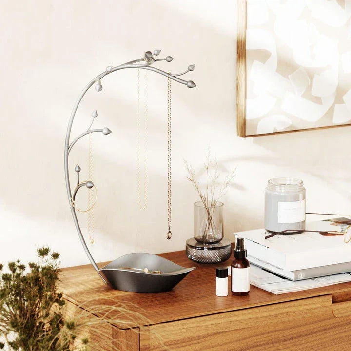 Modern jewelry organizer by Umbra with a tree-shaped design, displayed on a wooden dresser holding necklaces and rings.