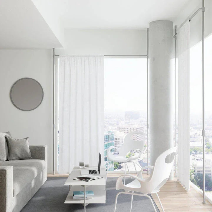 Modern curtain rods by Umbra installed in a bright, minimalist living room with floor-to-ceiling windows and sheer white curtains.