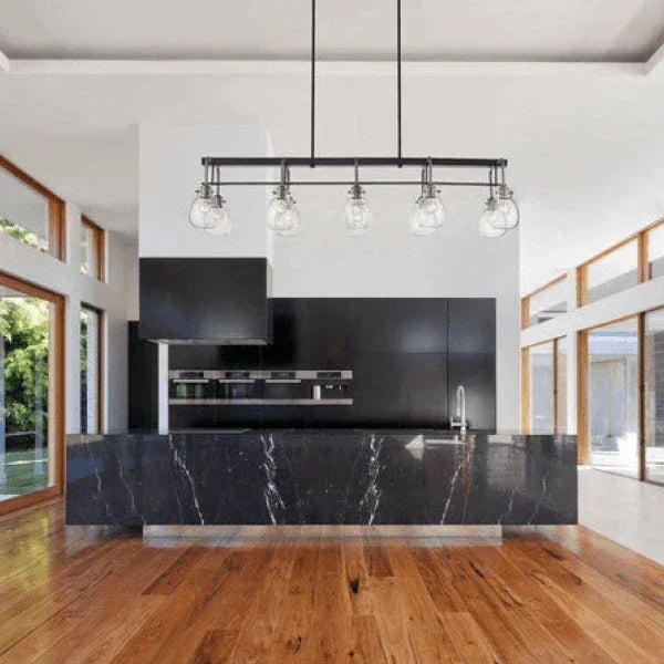 Z-Lite linear suspension lighting fixture hanging over a modern kitchen island with black countertops and wood flooring.