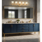 A double-sink bathroom vanity in deep navy blue with gold hardware, a white marble countertop, and a large matching rectangular mirror with a gold frame, set against a gray marble wall.