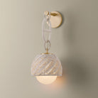 Piasu wall sconce illuminated, woven rattan shade glowing warm on gold brass chain link bracket with globe light below