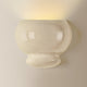 White ceramic bubble wall sconce mounted on wall, emitting warm upward light