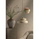 Styled room scene with cream disc pendant light on brass rod and ceramic bubble wall sconce, beside a vase with branches