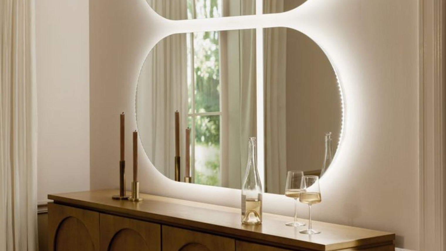 Large double circle backlit LED mirror with soft glow edge lighting above walnut sideboard in warm cream dining room