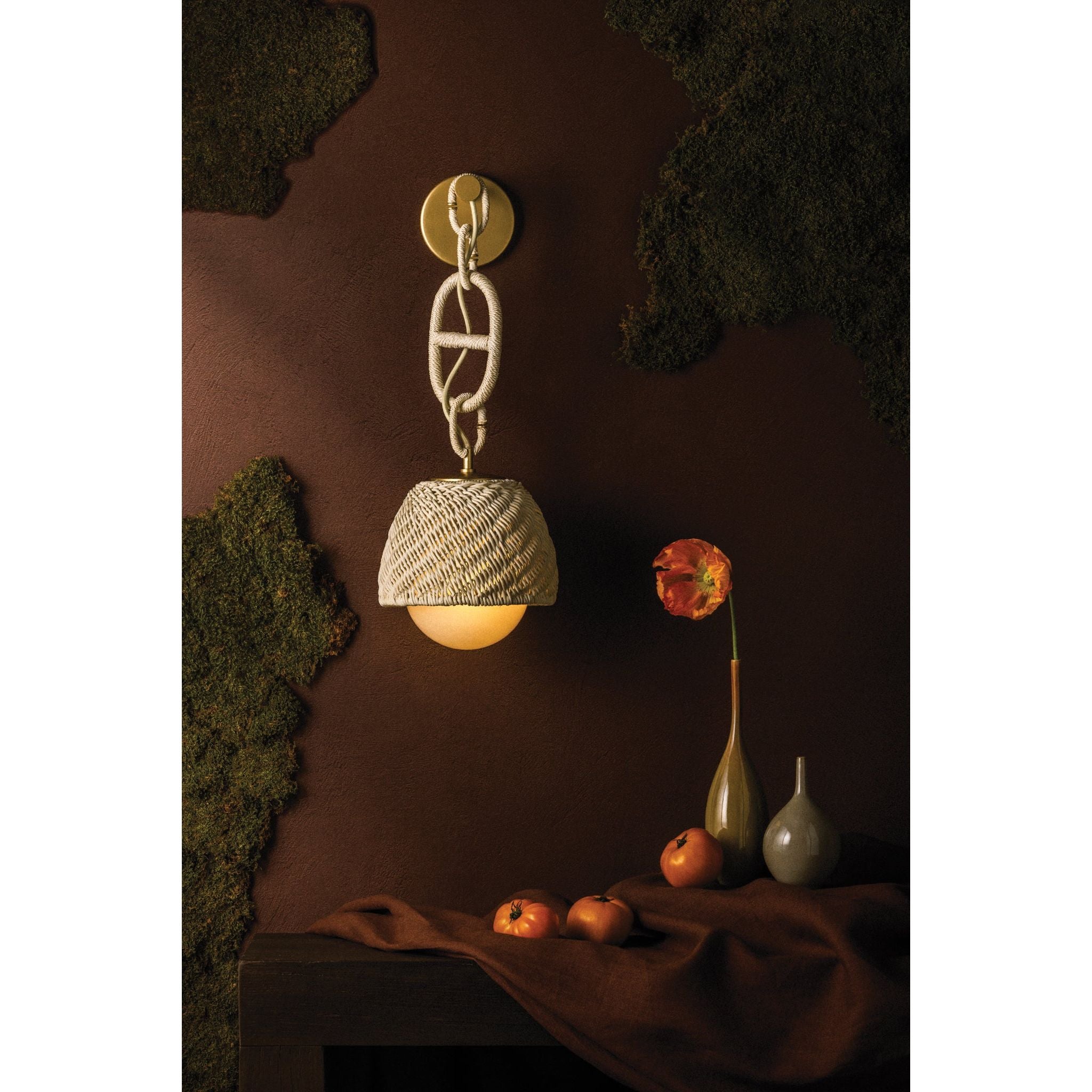 Piasu woven rattan wall sconce styled against dark brown wall with moss, decorative vase and florals