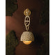 Piasu woven rattan wall sconce full view against dark wall with moss, showing gold chain links and globe diffuser below