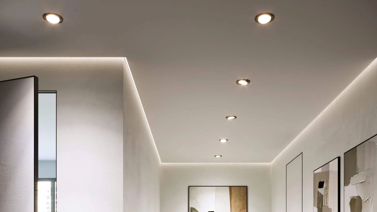 Row of recessed LED pot lights with LED strip cove lighting along white hallway ceiling above gallery wall in modern interior