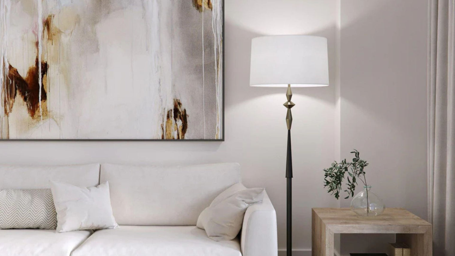 Antique brass and black turned column floor lamp with white drum shade beside white sofa and large abstract canvas in contemporary living room