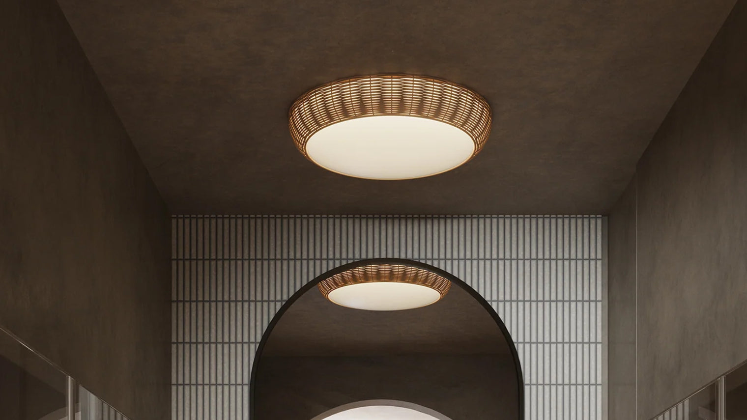 Round woven rattan flush mount ceiling light with large opal diffuser in moody hallway with arched doorway and ribbed tile wall