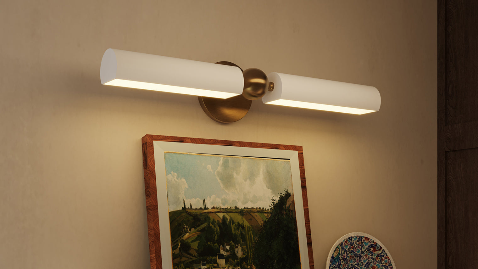 Antique brass double-arm pivot wall sconce with twin white tubular LED shades above framed landscape painting