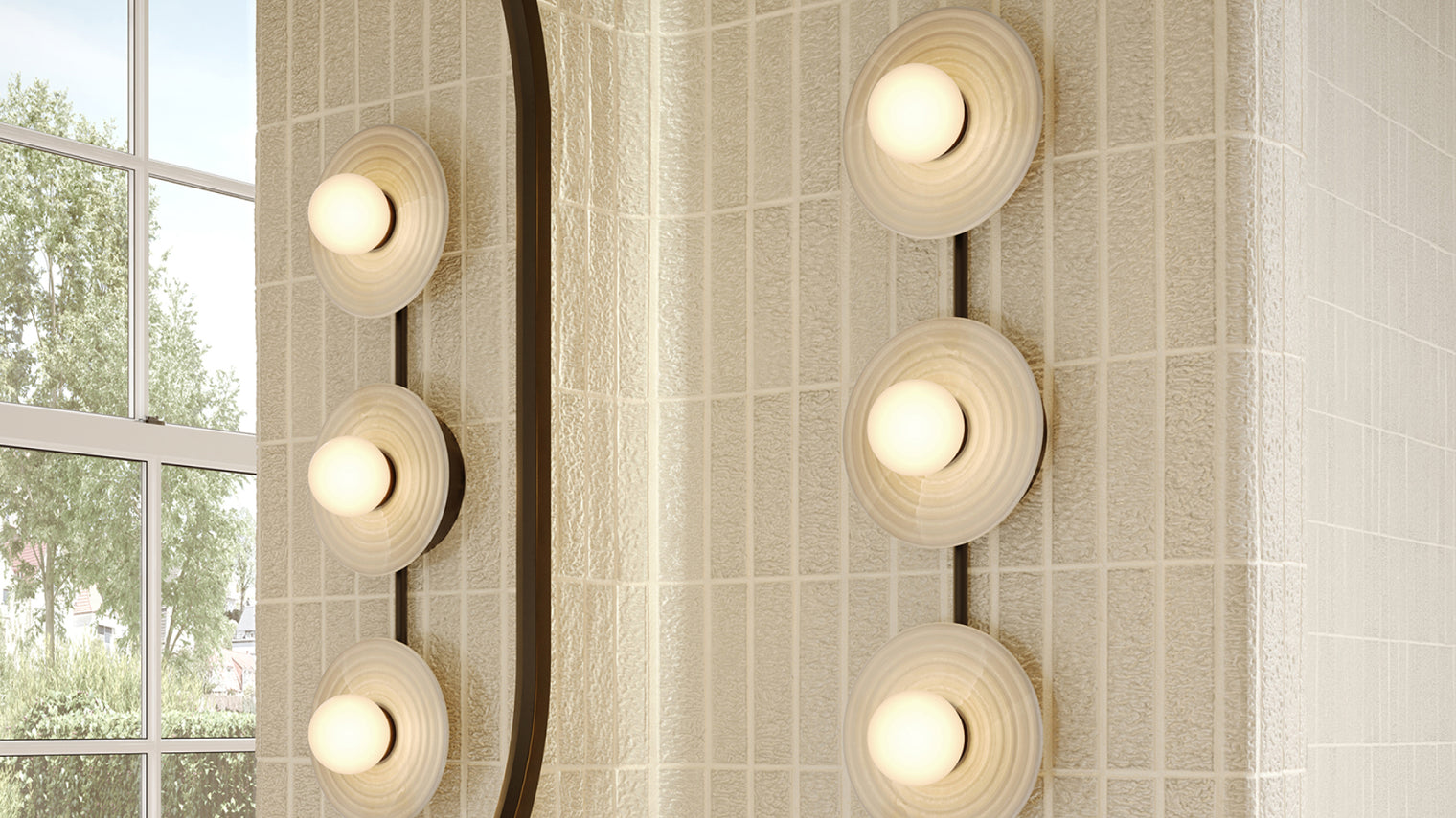 Stacked vertical bronze vanity bar with ribbed opal disc sconces mounted beside arched mirror on textured cream tile bathroom wall